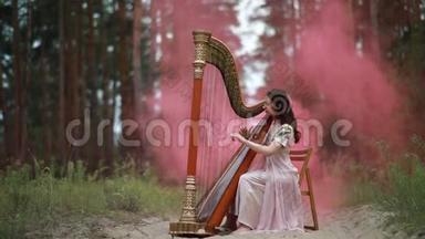 女<strong>竖琴</strong>手坐在森林里，在粉红色的烟雾的背景上弹奏<strong>竖琴</strong>。